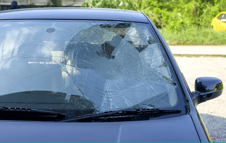 A broken windshield on the side of a blue car.