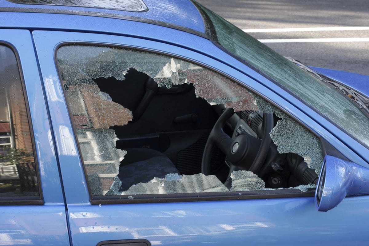 A blue car with a broken windshield and a hole in the window.